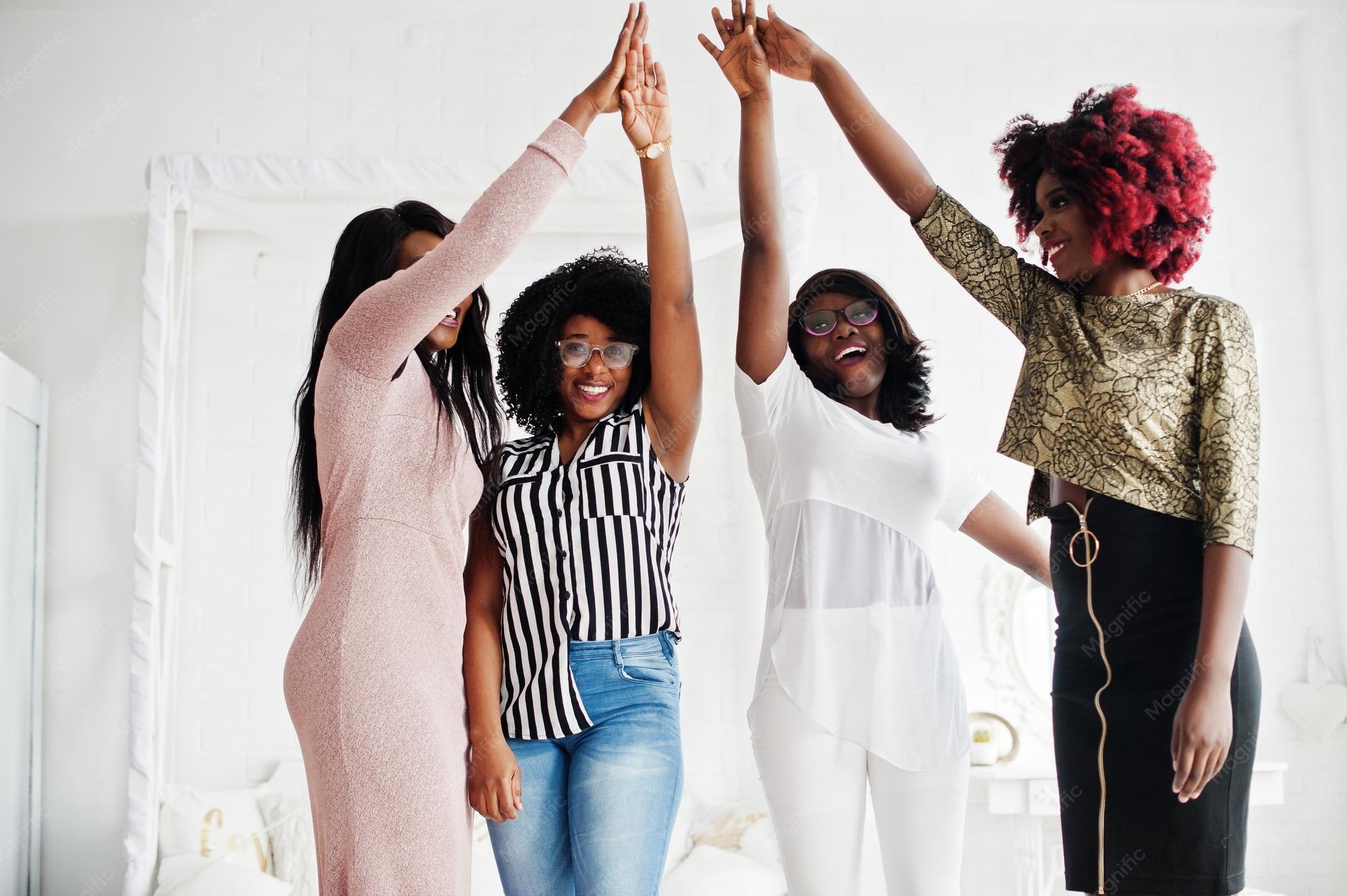 Four young African women friends stacking hands and celebrating together